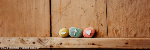 Steine mit Fisch, Kreuz und Herz an Holzwand